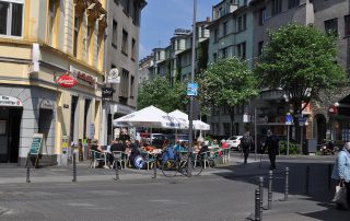 Mehrere Menschen sitzen vor einem Restaurant unter Sonnenschirmen