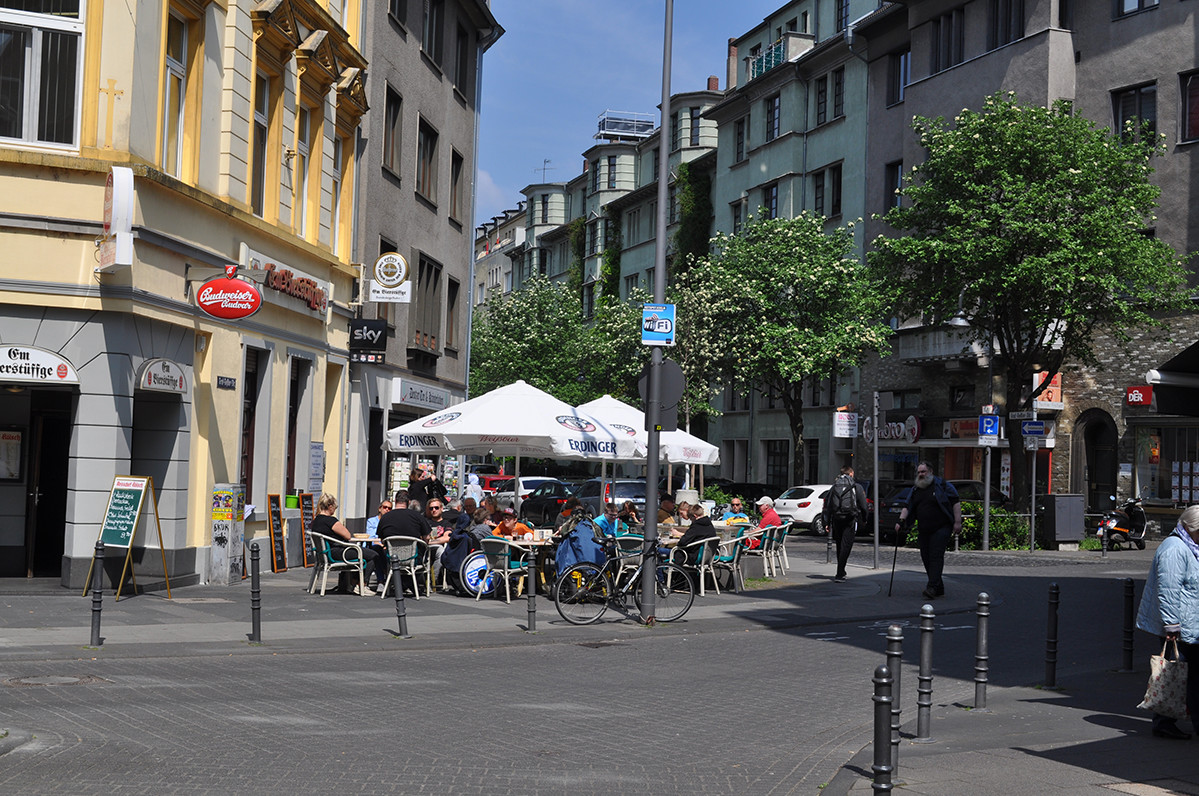 Mehrere Menschen sitzen vor einem Restaurant unter Sonnenschirmen